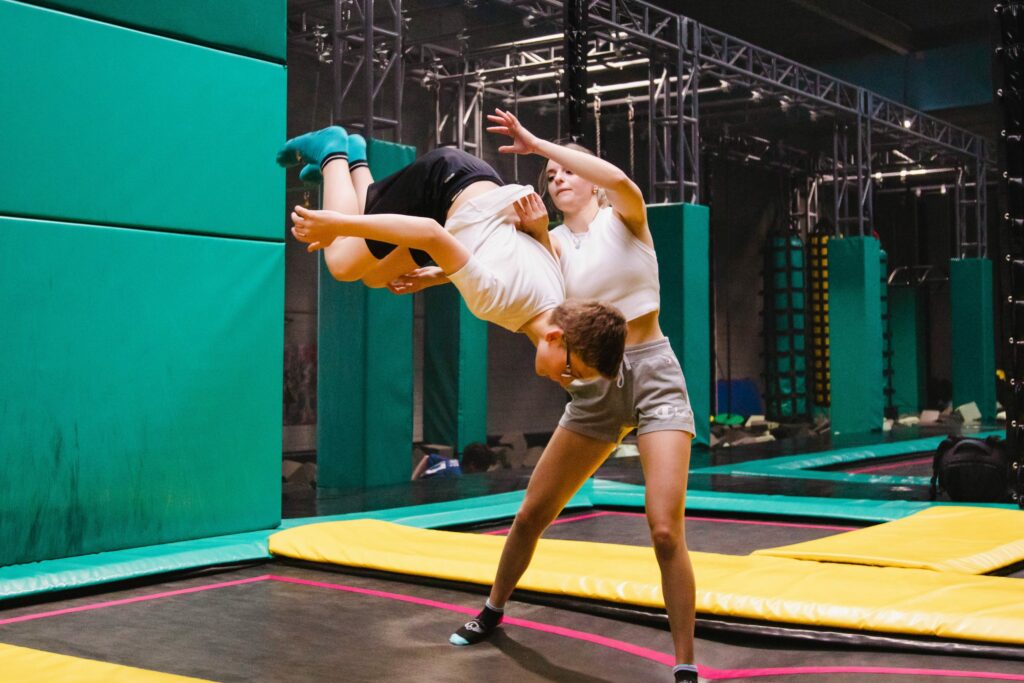 Adulte aidant un enfant à faire une pirouette sur trampoline dans un espace de jeux